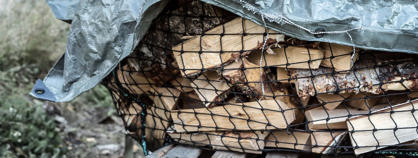 Stored firewood outside covered by a tarp.