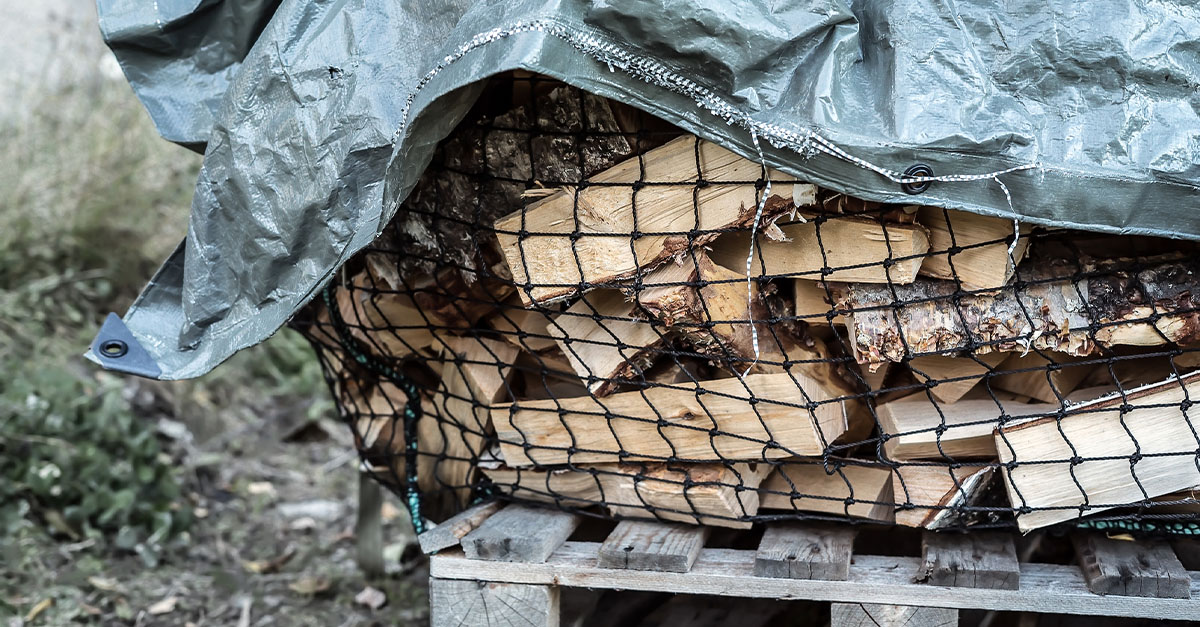 Stored firewood outside covered by a tarp.